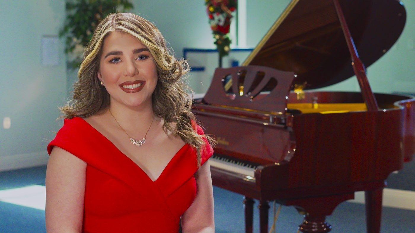 Elizabeth con vestido rojo junto a un piano de cola